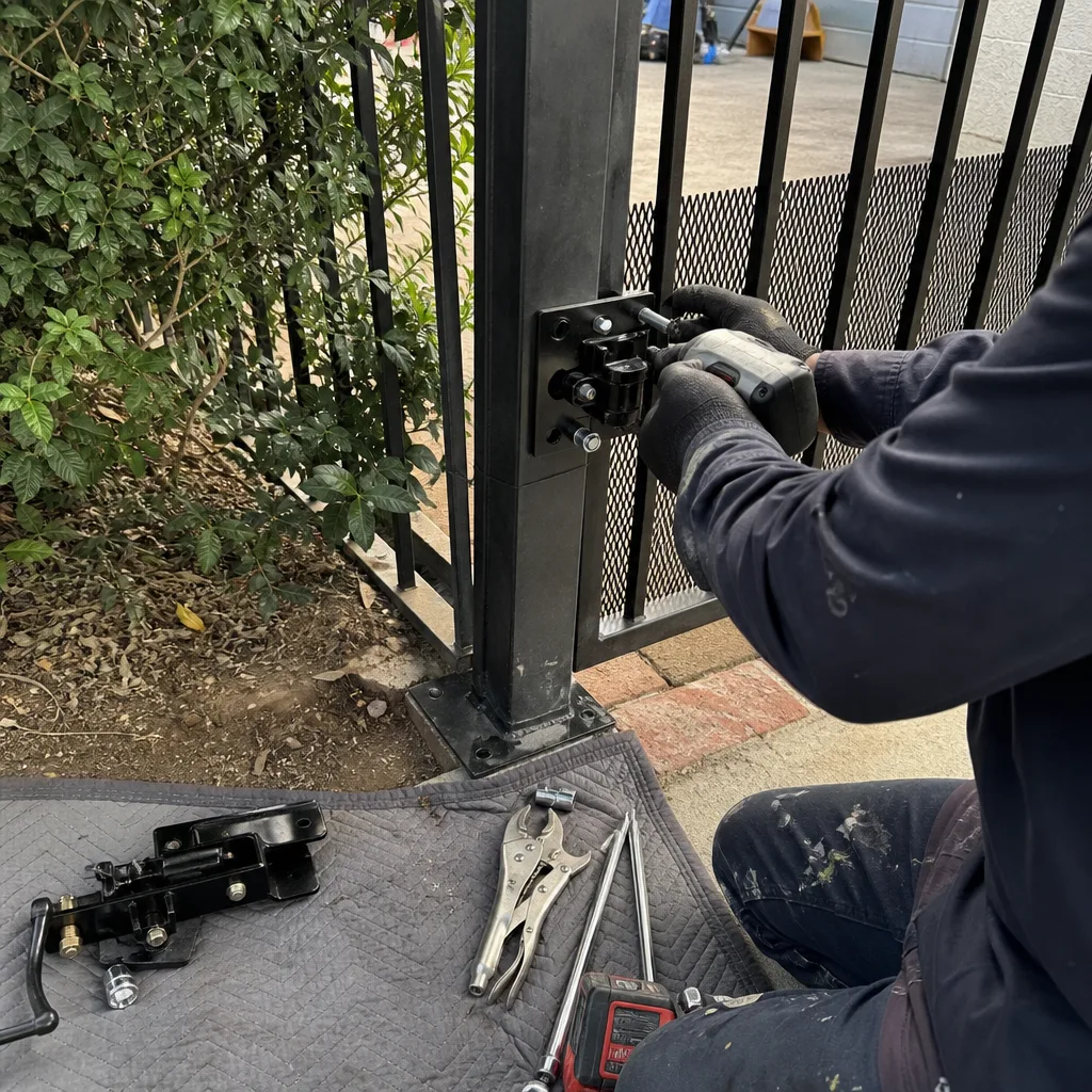 Technician using a power drill to repair a black metal gate hinge